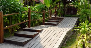 Umgeben von Grünpflanzen führen Treppenstufen bergauf, rechts daneben befindet sich eine Rampe.